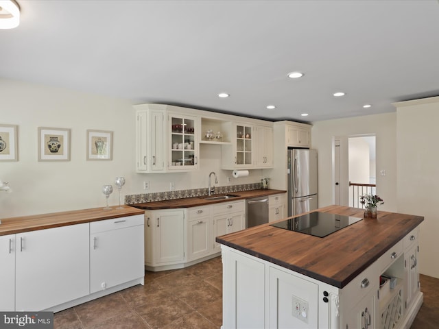 kitchen with glass insert cabinets, butcher block counters, recessed lighting, appliances with stainless steel finishes, and a sink