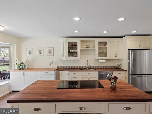 kitchen with butcher block countertops, glass insert cabinets, a center island, appliances with stainless steel finishes, and a sink