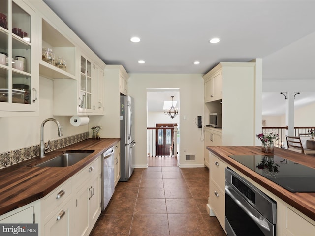 kitchen with visible vents, glass insert cabinets, a sink, appliances with stainless steel finishes, and butcher block counters