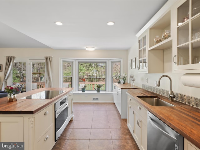 kitchen featuring glass insert cabinets, a sink, stainless steel appliances, butcher block countertops, and tile patterned flooring