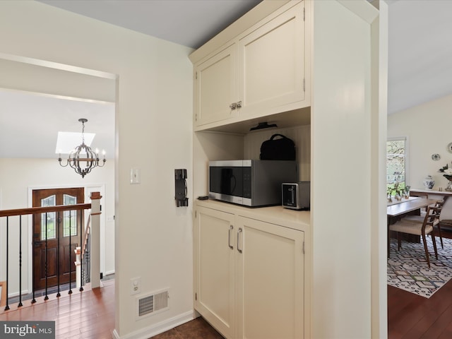 kitchen with stainless steel microwave, a notable chandelier, baseboards, dark wood-style flooring, and visible vents