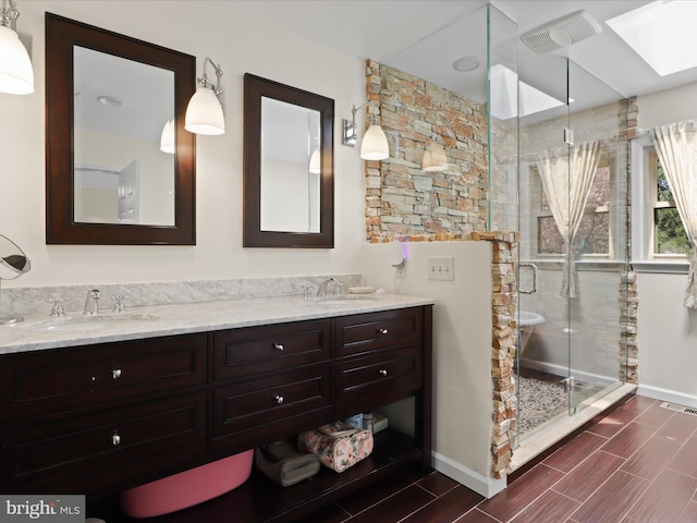 bathroom with a stall shower, double vanity, a sink, and wood finish floors