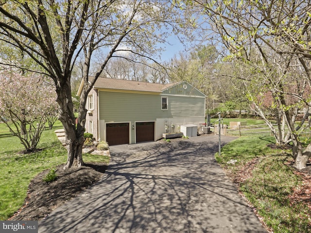 view of side of property featuring a garage, driveway, fence, and a lawn