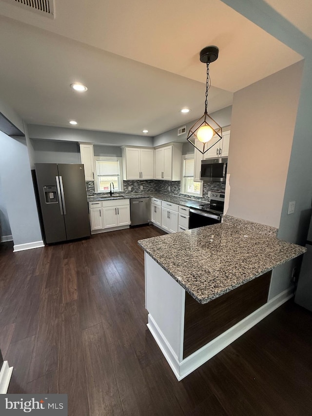 kitchen with white cabinets, a peninsula, a sink, dark stone countertops, and appliances with stainless steel finishes