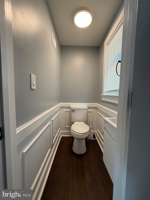 bathroom with toilet, wainscoting, visible vents, wood finished floors, and a decorative wall