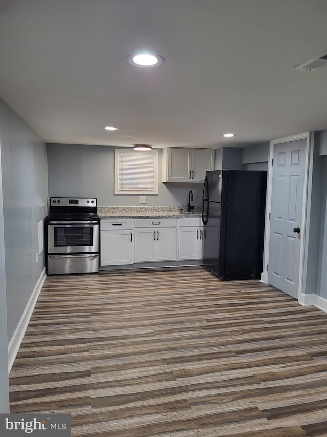 kitchen featuring dark wood-style flooring, stainless steel range with electric cooktop, baseboards, freestanding refrigerator, and light stone counters
