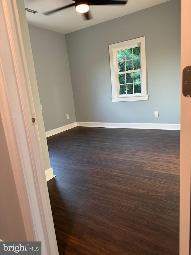 spare room featuring ceiling fan, baseboards, and dark wood-style flooring