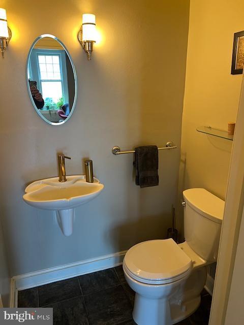 half bathroom with toilet, tile patterned flooring, and baseboards