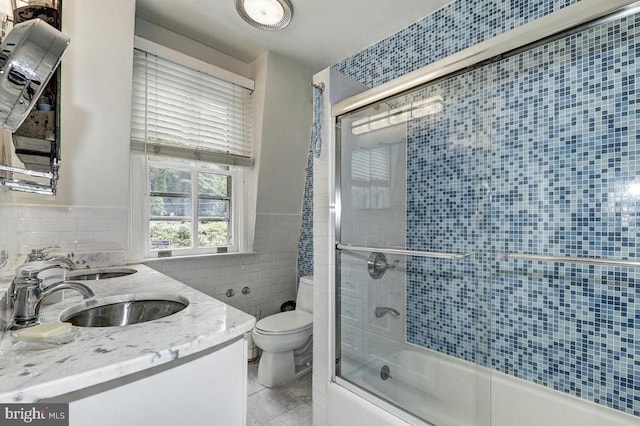 full bath featuring tile walls, combined bath / shower with glass door, toilet, double vanity, and tile patterned floors