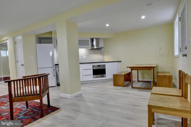 kitchen with stainless steel oven, freestanding refrigerator, wall chimney range hood, baseboards, and backsplash