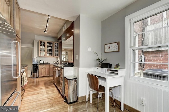 kitchen featuring stainless steel appliances, light wood finished floors, track lighting, wainscoting, and glass insert cabinets