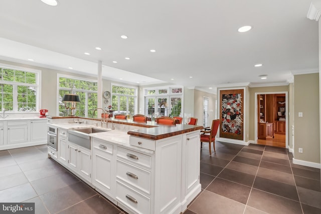 kitchen with a sink, a spacious island, ornamental molding, dark tile patterned flooring, and stainless steel oven