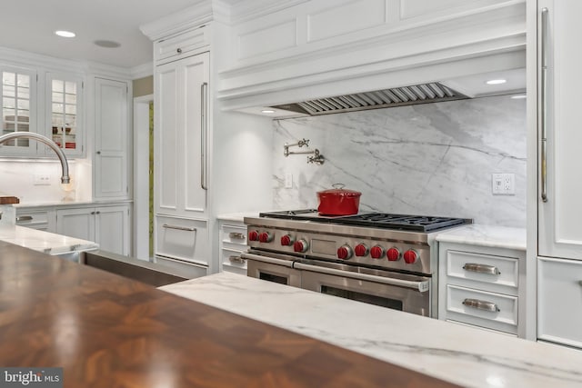 interior space with light stone countertops, custom exhaust hood, backsplash, double oven range, and white cabinets