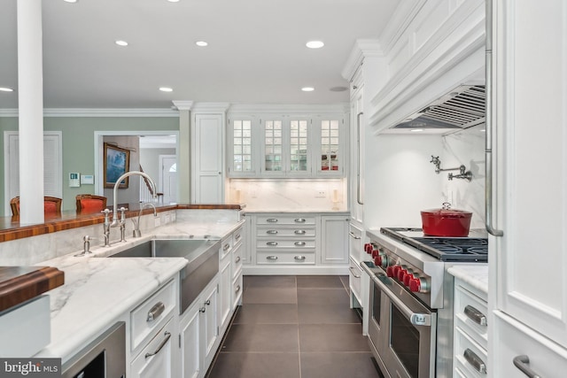 kitchen featuring double oven range, white cabinets, custom range hood, and a sink