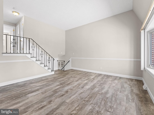 unfurnished living room featuring wood finished floors, lofted ceiling, and baseboards