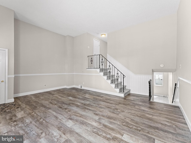 unfurnished living room featuring stairs, wood finished floors, and baseboards