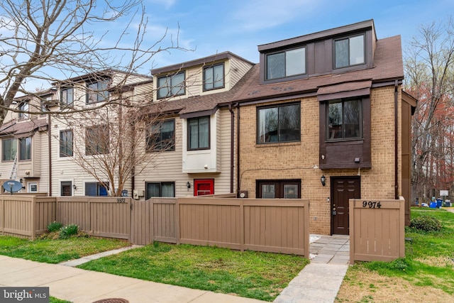 multi unit property with brick siding, roof with shingles, and a fenced front yard