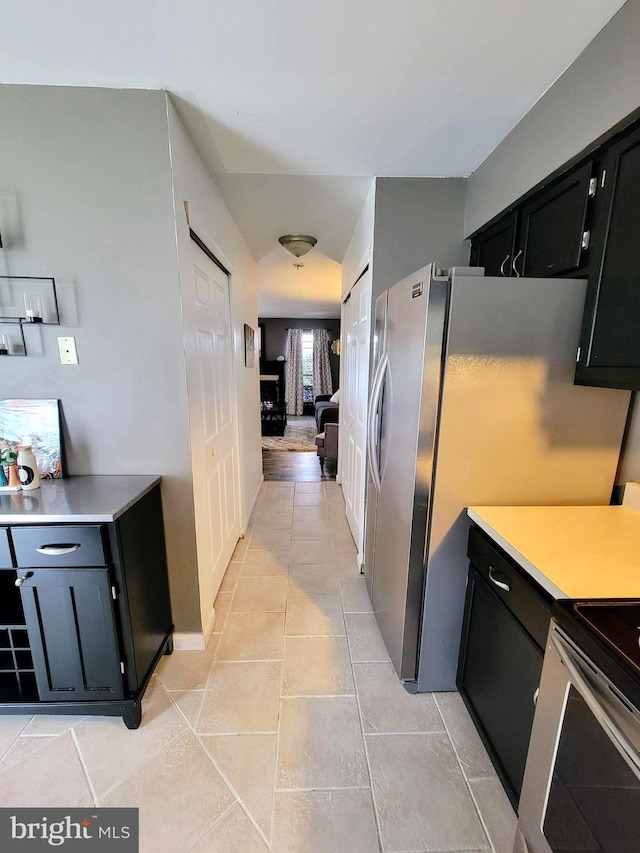 kitchen with light countertops, freestanding refrigerator, light tile patterned flooring, and dark cabinets