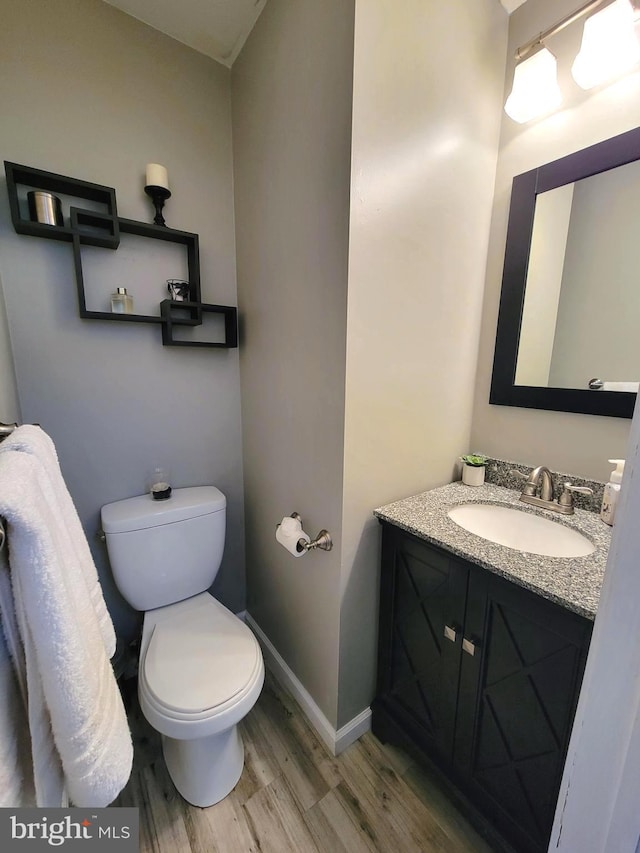 half bathroom featuring toilet, vanity, wood finished floors, and baseboards