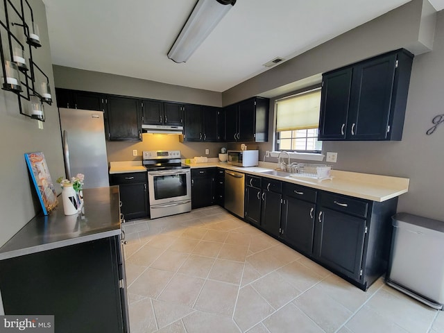 kitchen featuring dark cabinetry, appliances with stainless steel finishes, light countertops, and under cabinet range hood