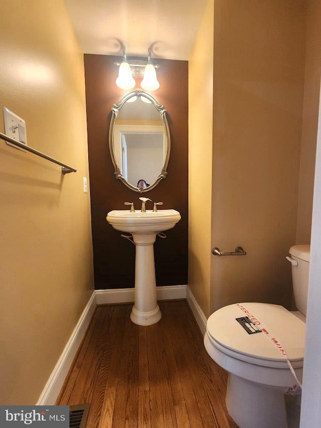 half bathroom with baseboards, visible vents, toilet, and wood finished floors
