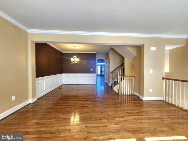 empty room with stairway, ornamental molding, arched walkways, a notable chandelier, and wood finished floors
