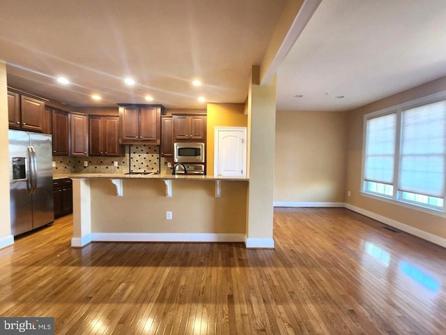 kitchen with hardwood / wood-style flooring, tasteful backsplash, appliances with stainless steel finishes, a sink, and a breakfast bar area