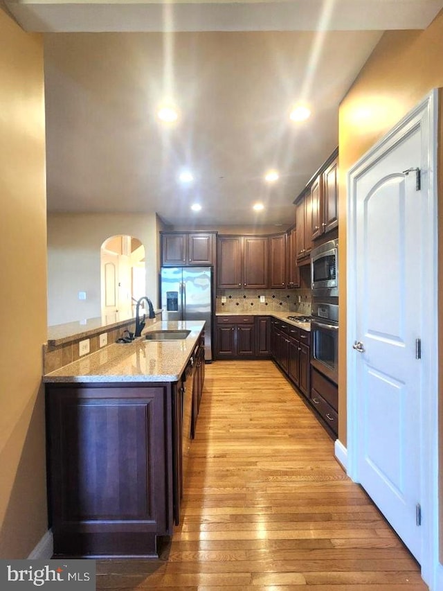 kitchen featuring decorative backsplash, dark brown cabinets, appliances with stainless steel finishes, arched walkways, and a sink