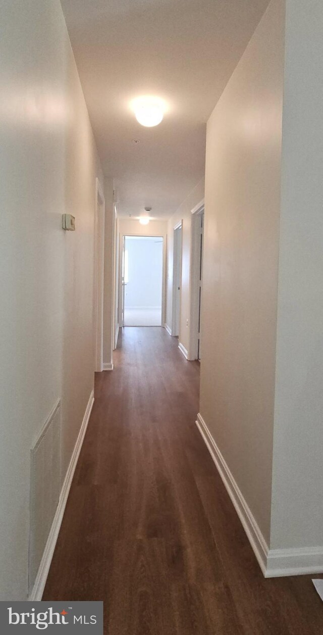 hallway featuring dark wood-type flooring, baseboards, and visible vents