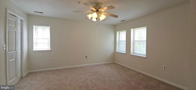 empty room with visible vents, baseboards, ceiling fan, and light carpet