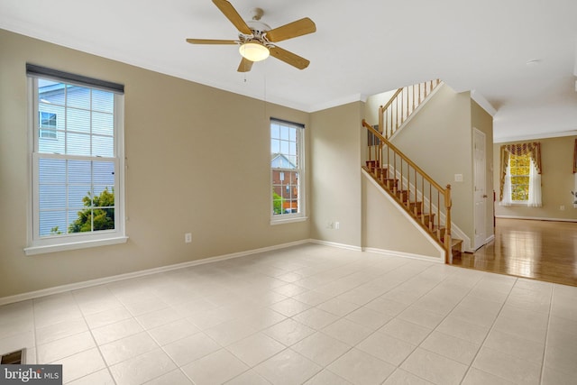 empty room featuring crown molding, ceiling fan, baseboards, and stairs
