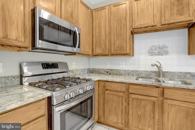 kitchen featuring light stone countertops, stainless steel appliances, a sink, and backsplash