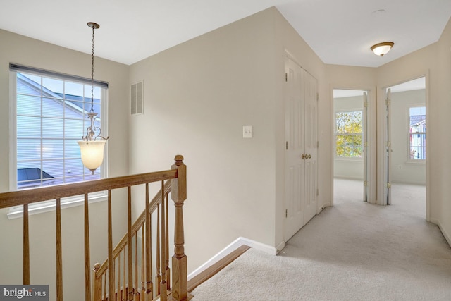 hallway with visible vents, baseboards, an upstairs landing, and plenty of natural light