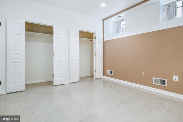 unfurnished bedroom with two closets, concrete floors, and visible vents