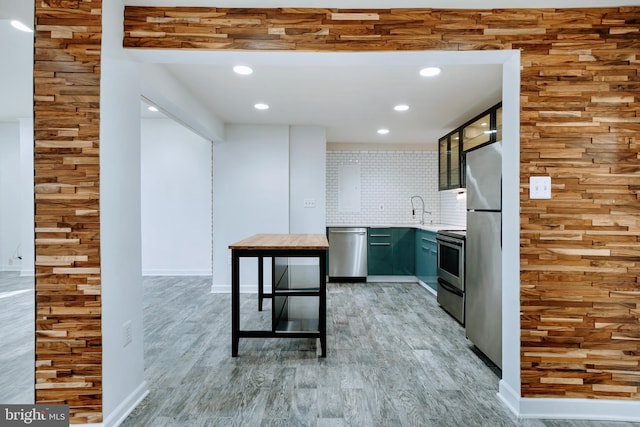 kitchen with appliances with stainless steel finishes, light countertops, recessed lighting, light wood-type flooring, and backsplash
