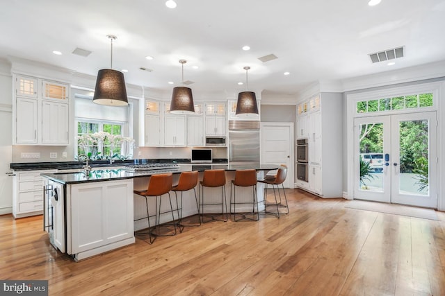 kitchen with dark countertops, built in appliances, white cabinetry, recessed lighting, and a large island with sink