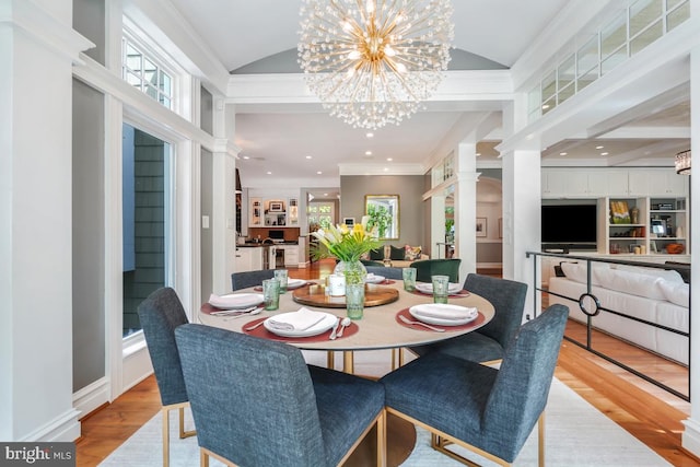 dining area with a chandelier, wood finished floors, ornate columns, vaulted ceiling, and ornamental molding