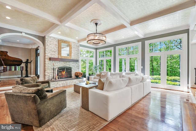 living room featuring arched walkways, beamed ceiling, a stone fireplace, and wood finished floors