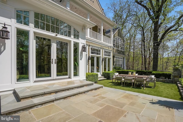 rear view of property with french doors, outdoor dining area, a lawn, a balcony, and a patio