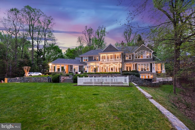back of house at dusk with a yard, a chimney, and a balcony