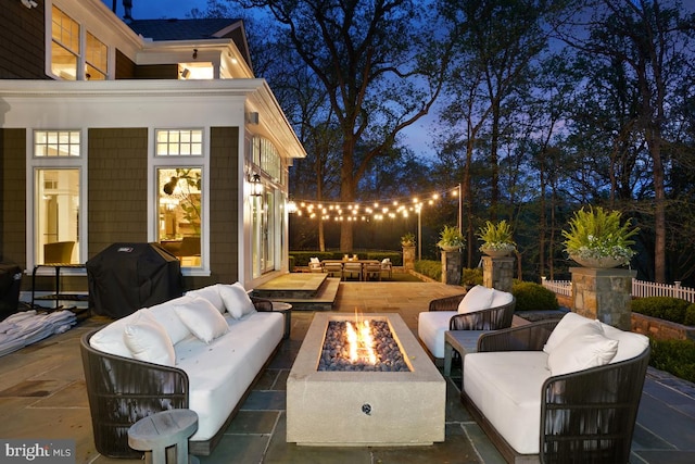 patio at night with an outdoor living space with a fire pit and area for grilling