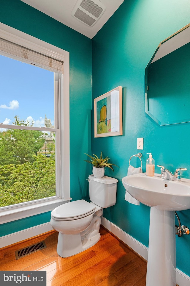 half bath with toilet, baseboards, wood finished floors, and healthy amount of natural light