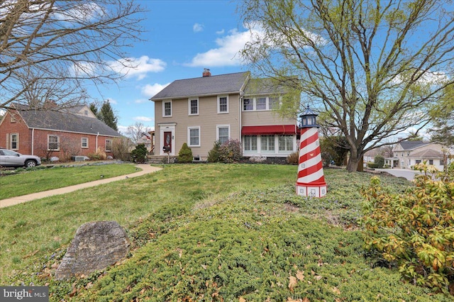 colonial home featuring a chimney, a residential view, and a front lawn
