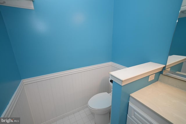 half bath featuring tile patterned flooring, toilet, wainscoting, and vanity