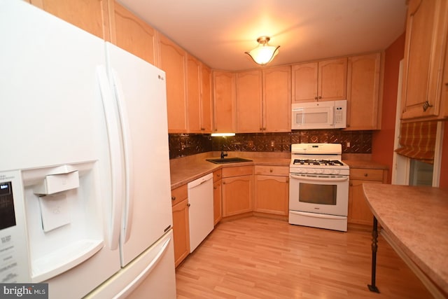 kitchen featuring light wood finished floors, decorative backsplash, a sink, and white appliances