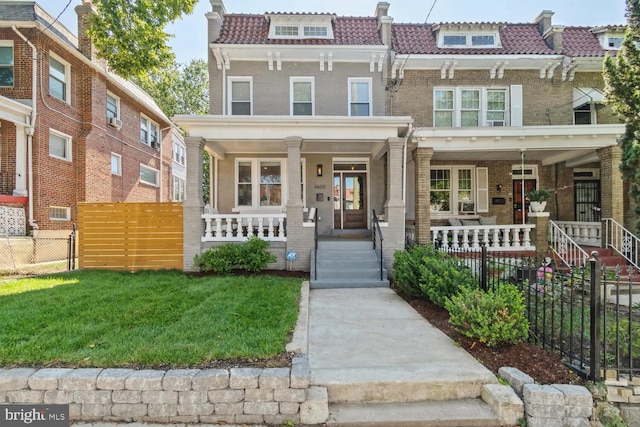view of front of property with mansard roof, a front yard, brick siding, a porch, and fence