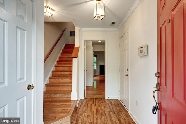 entryway with light wood-type flooring, visible vents, baseboards, ornamental molding, and stairs