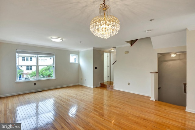 empty room with visible vents, baseboards, light wood-style floors, a chandelier, and ornamental molding