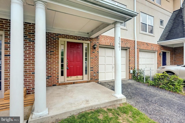 view of exterior entry with stucco siding, brick siding, covered porch, and a garage