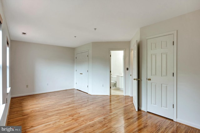 unfurnished bedroom with baseboards, ensuite bath, visible vents, and light wood-type flooring